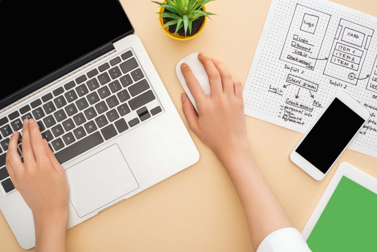 partial view of designer using laptop near gadgets, website design template and green plant on beige